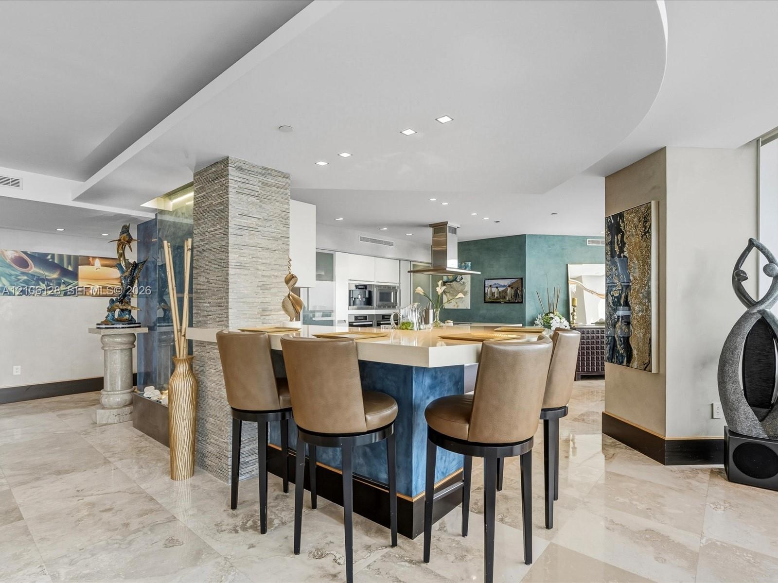 Custom kitchen island with a stone-finish countertop and blue cabinetry, textured stone accent pillar, recessed ceiling lighting, and polished stone f