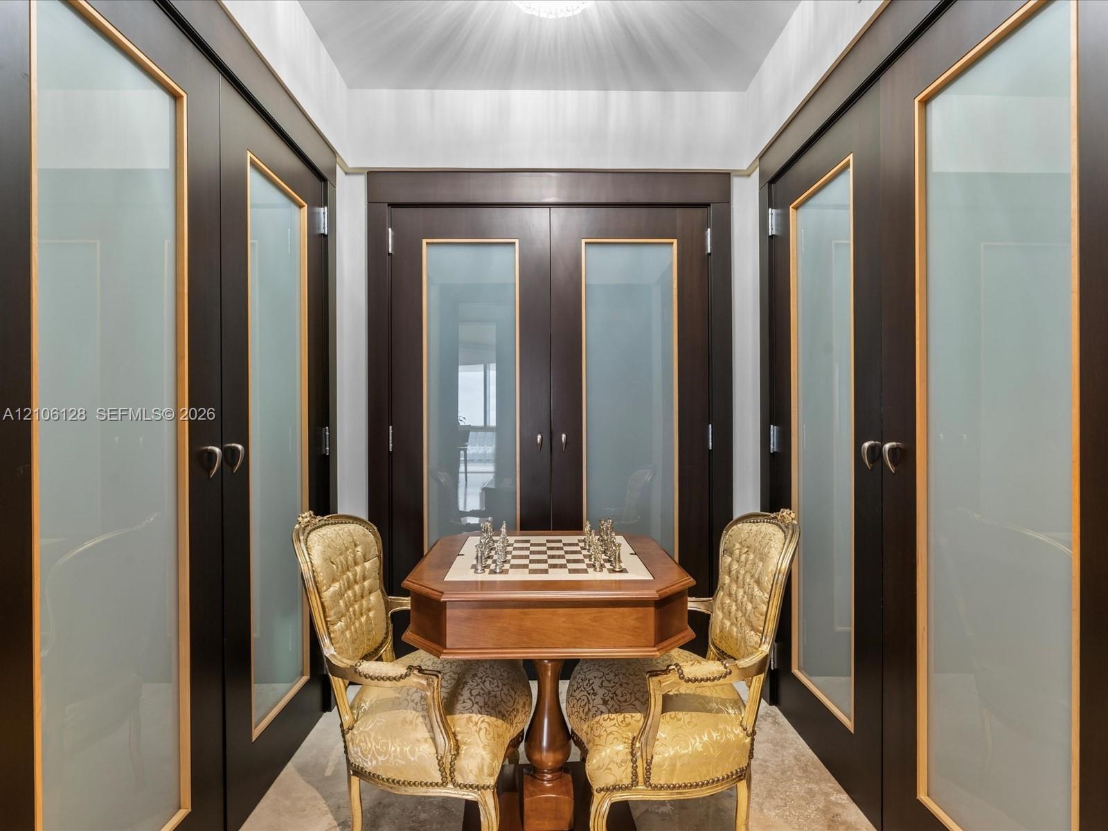 Dark-finish built-in cabinetry featuring frosted glass panels with gold-tone trim, crown molding, and stone flooring