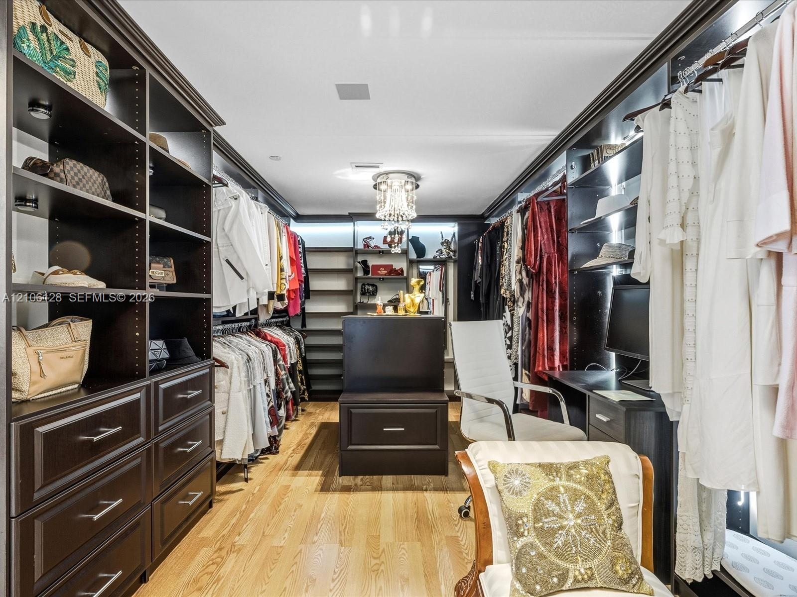 Custom walk-in closet featuring floor-to-ceiling dark wood cabinetry, integrated storage island with drawers, built-in desk workstation, wood-finish f