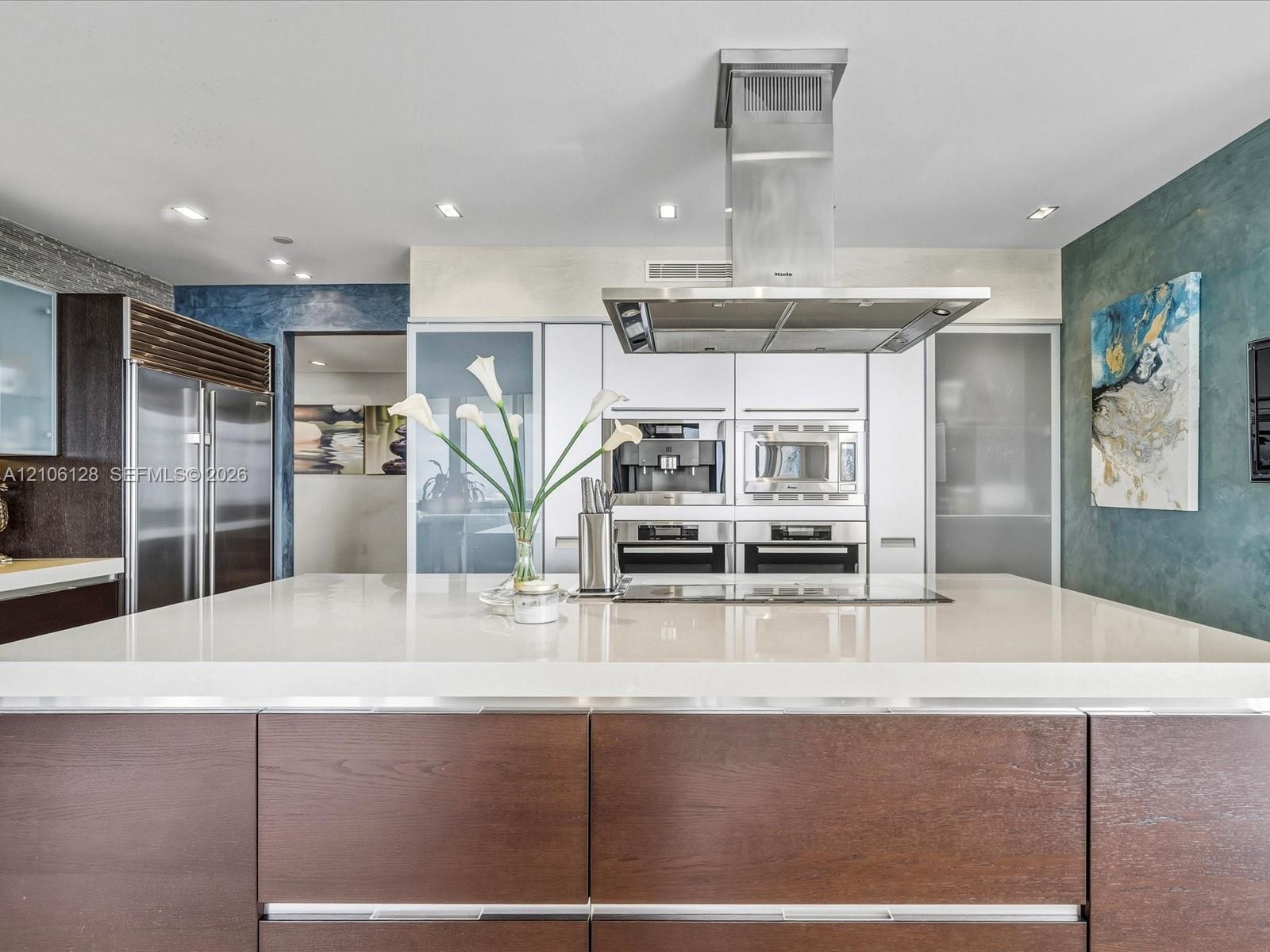 Kitchen featuring a large central island with a quartz countertop, flat-panel wood-finish cabinetry, built-in stainless steel appliances, and a ceilin
