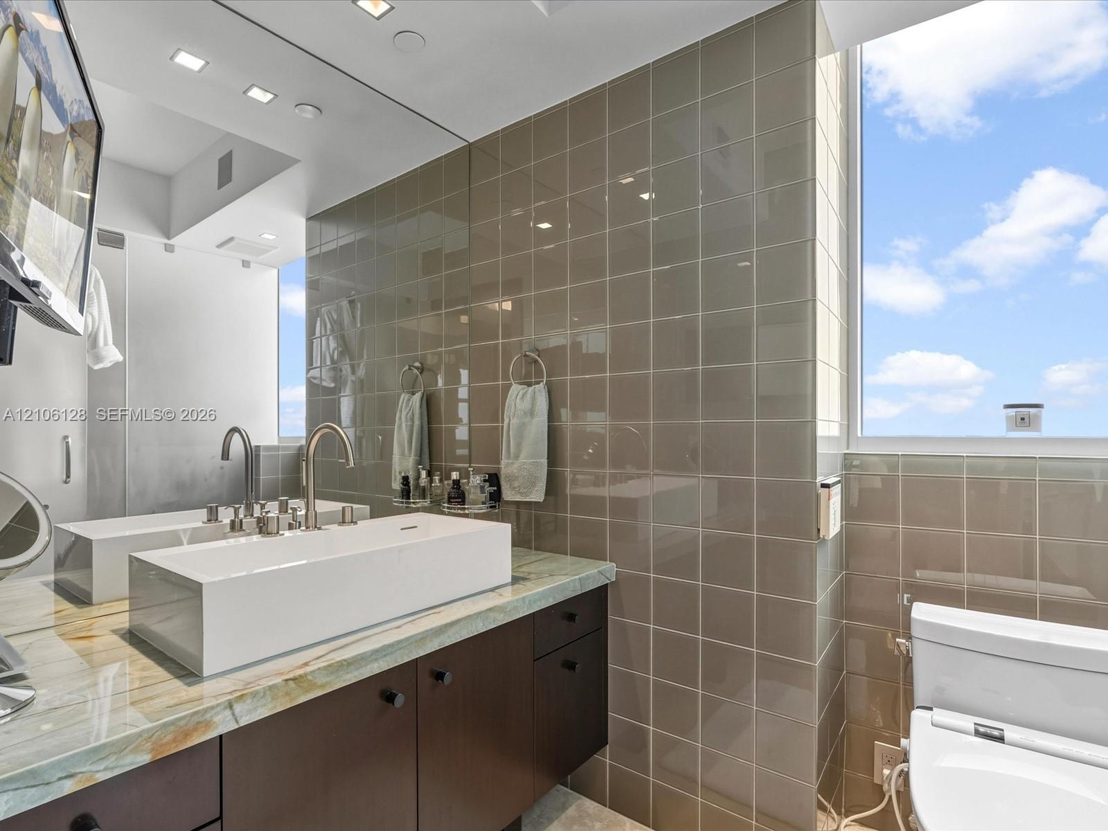 Floating vanity with rectangular vessel sinks, stone countertop, gloss-finish wall tile, and recessed lighting