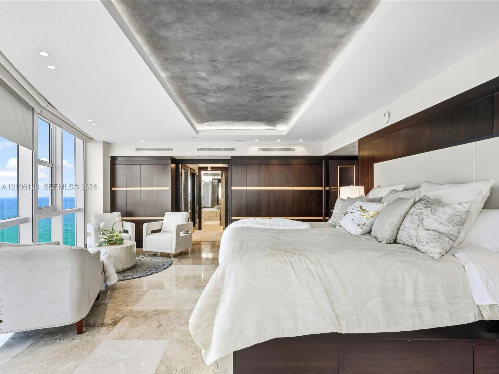 Floor-to-ceiling windows, custom dark wood-finish wall paneling, recessed tray ceiling with integrated lighting, and polished stone flooring