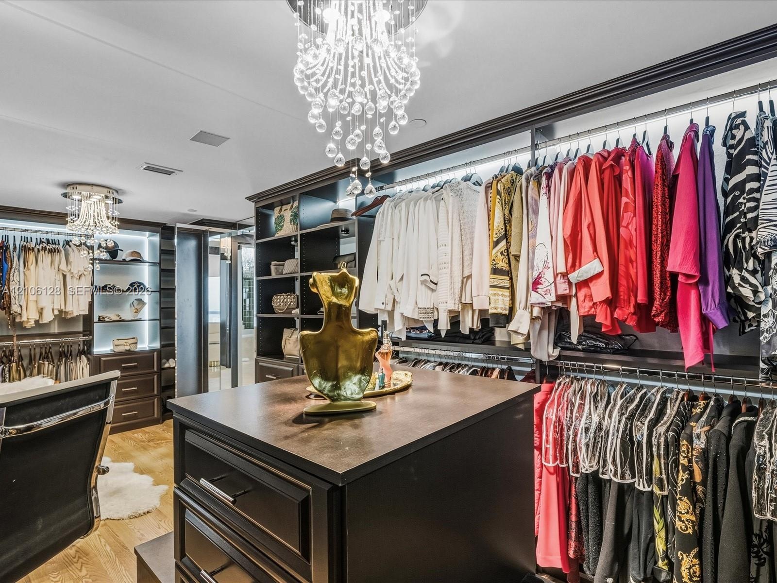 Custom walk-in closet featuring built-in dark wood cabinetry, integrated LED shelf lighting, a center island with a dark countertop, and decorative cr