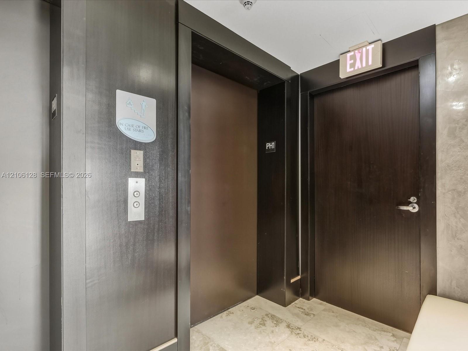Elevator landing featuring dark wood-finish door frames, a metallic elevator door, and light-toned stone tile flooring