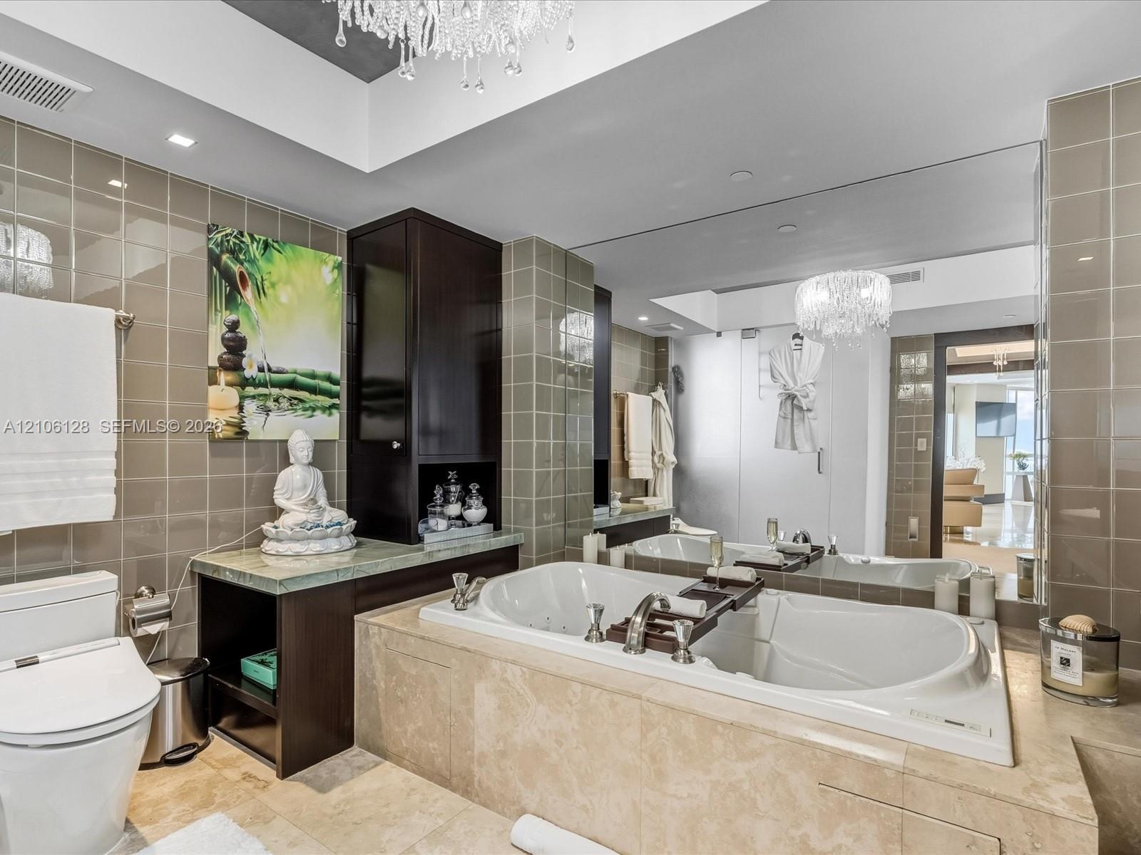 Bathroom featuring a stone-encased jetted soaking tub, dark-finish cabinetry with an integrated countertop, wall-to-wall mirror, tiled walls, and a cr