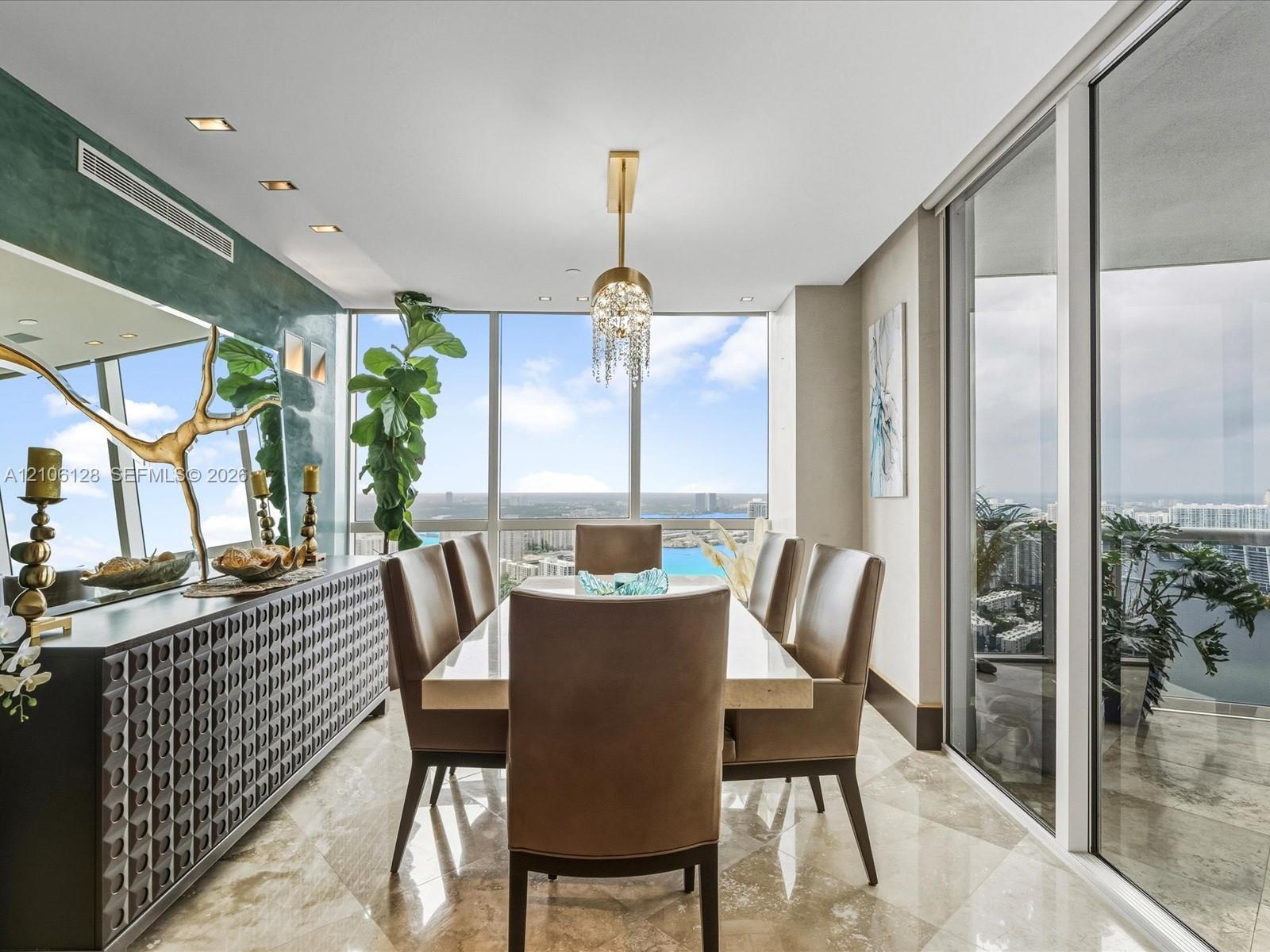 Floor-to-ceiling windows, polished stone flooring, recessed ceiling lighting, and a tiered crystal pendant fixture