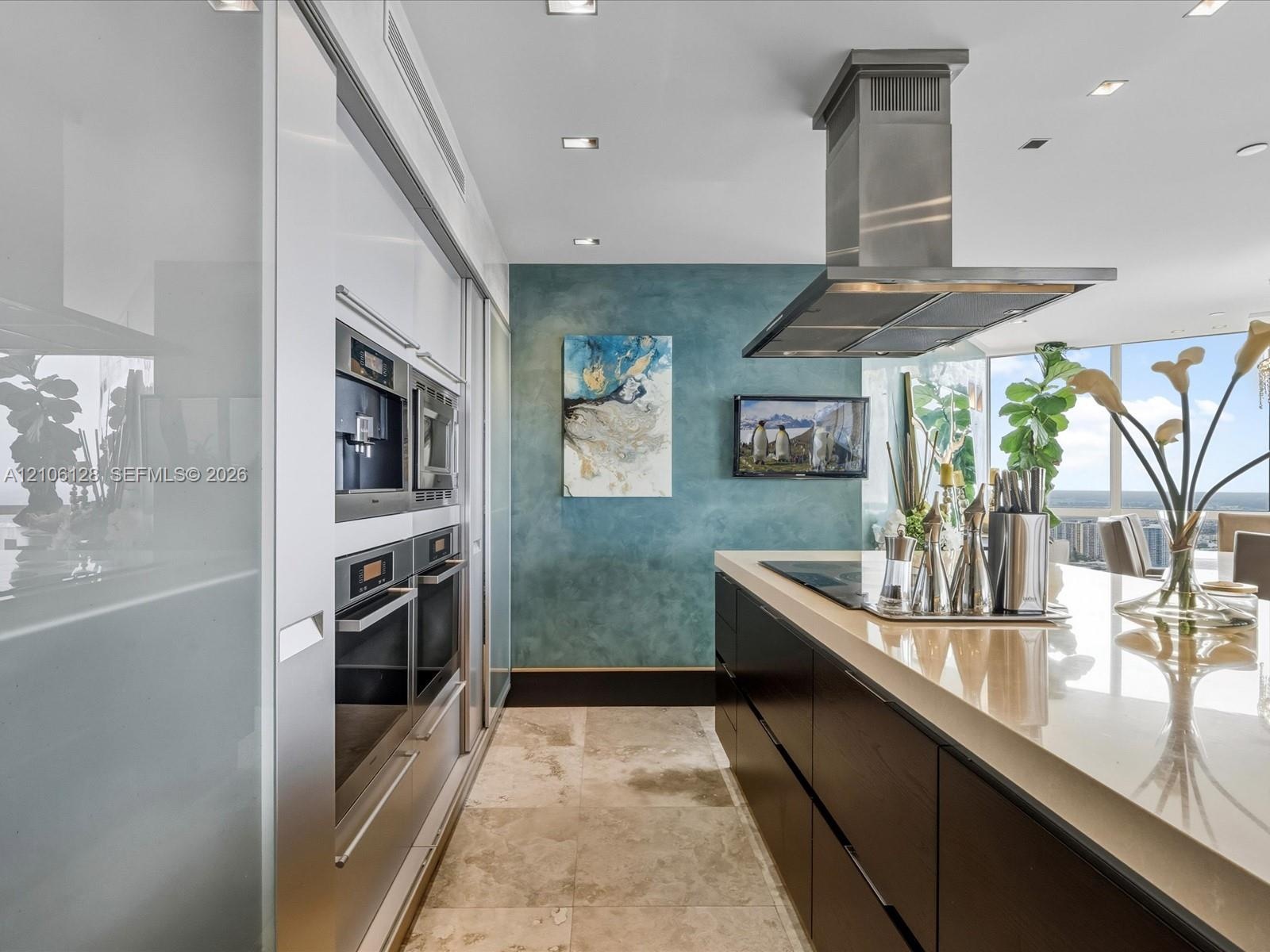 Kitchen featuring a central island with a stone countertop, built-in stainless steel wall ovens, floor-to-ceiling cabinetry, recessed lighting, and a 
