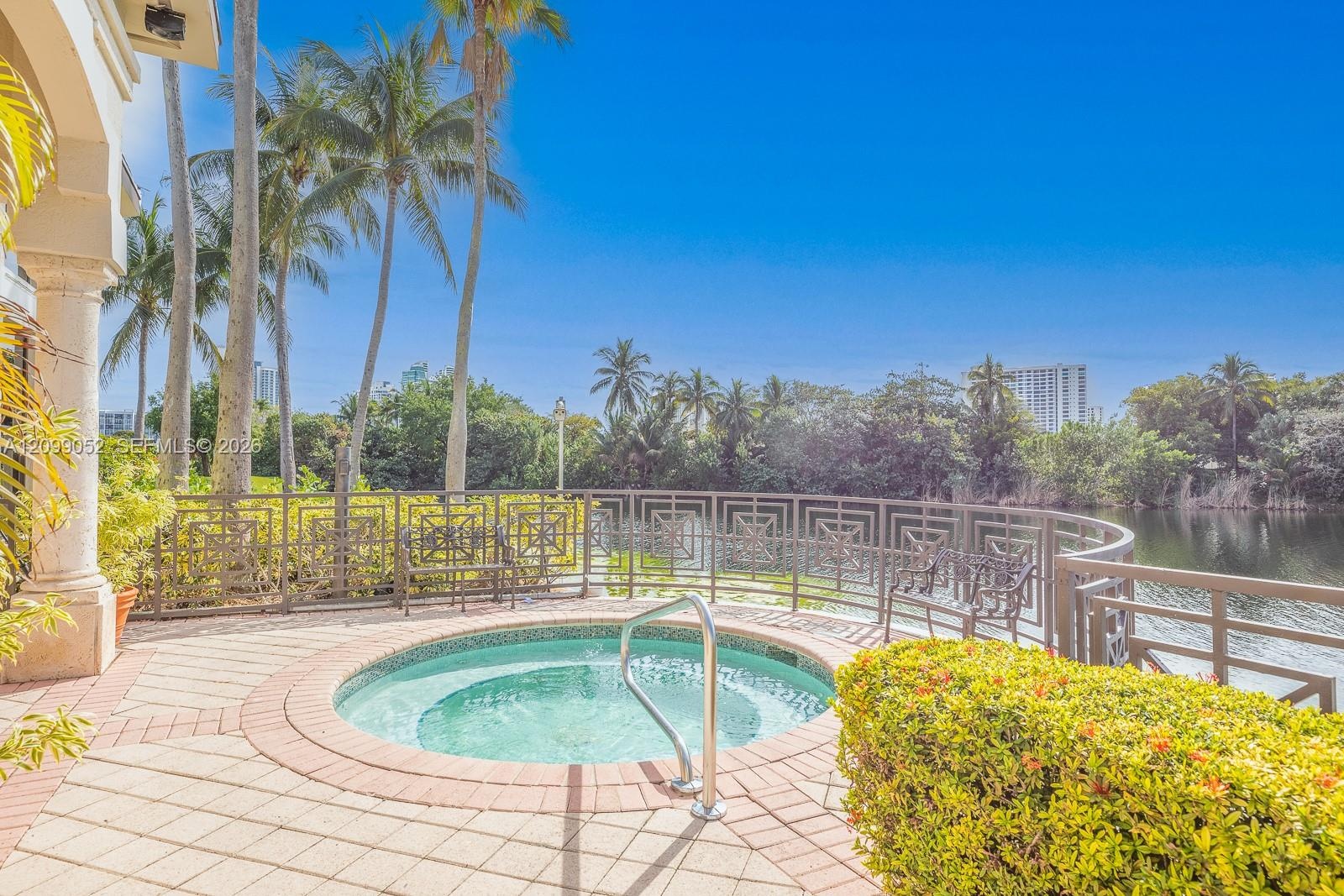 Circular in-ground spa featuring a tiled interior and stainless steel handrail, surrounded by a paved deck, decorative metal railing, and manicured la