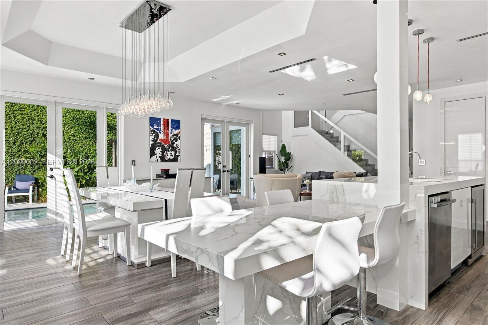 Open-concept interior featuring a coffered ceiling, stone-surfaced waterfall island, wood-finish flooring, glass pendant lighting, and multi-panel gla