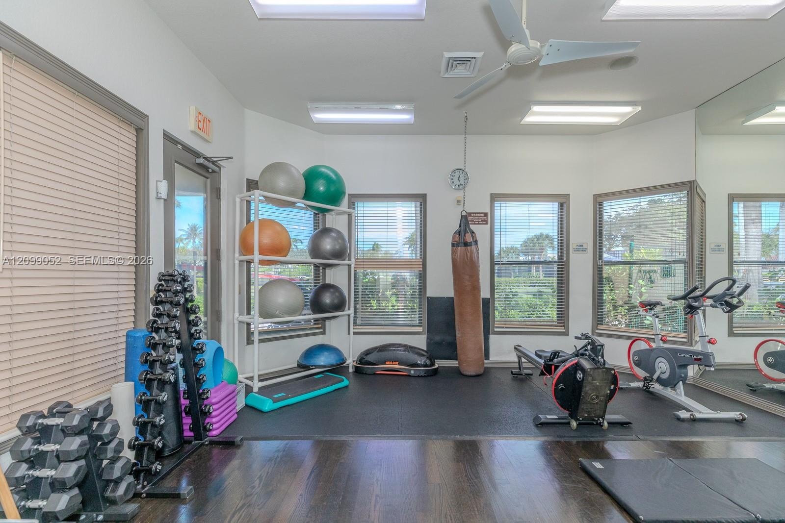Dedicated fitness area featuring dark wood-finish flooring, rubberized gym flooring, floor-to-ceiling wall mirror, recessed ceiling lighting, and mult