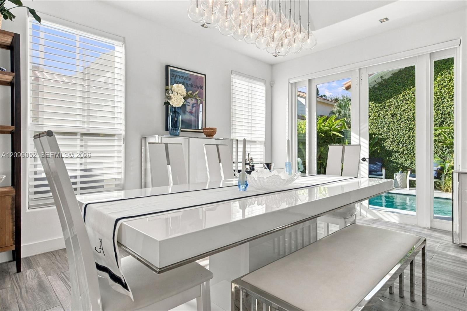 Dining area featuring large-format tile flooring, multi-globe chandelier, crisp white walls, horizontal window blinds, and glass doors opening to an o