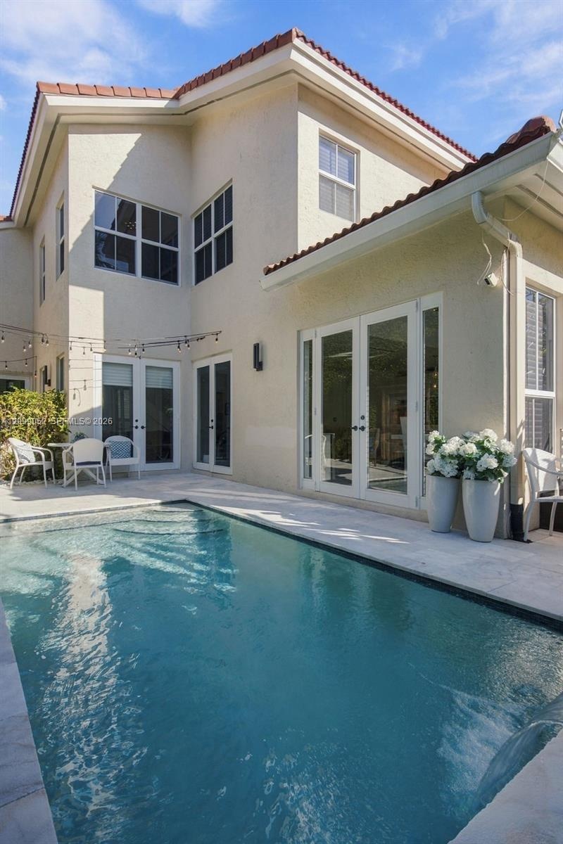 Stucco exterior with a tiled roof, featuring multiple sets of white-framed glass paneled doors and a private swimming pool with stone paver decking