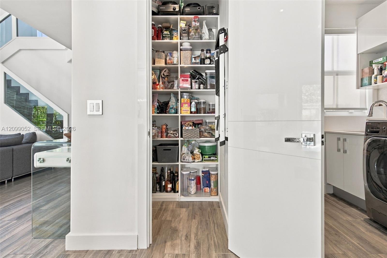 Walk-in pantry featuring floor-to-ceiling custom white shelving, high-gloss flat-panel door, and wood-finish flooring