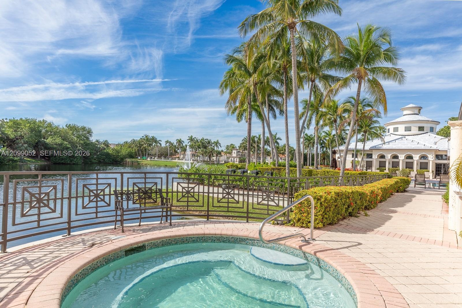 In-ground spa with stone-tiled interior, paver patio, decorative metal perimeter fencing, and mature palm trees
