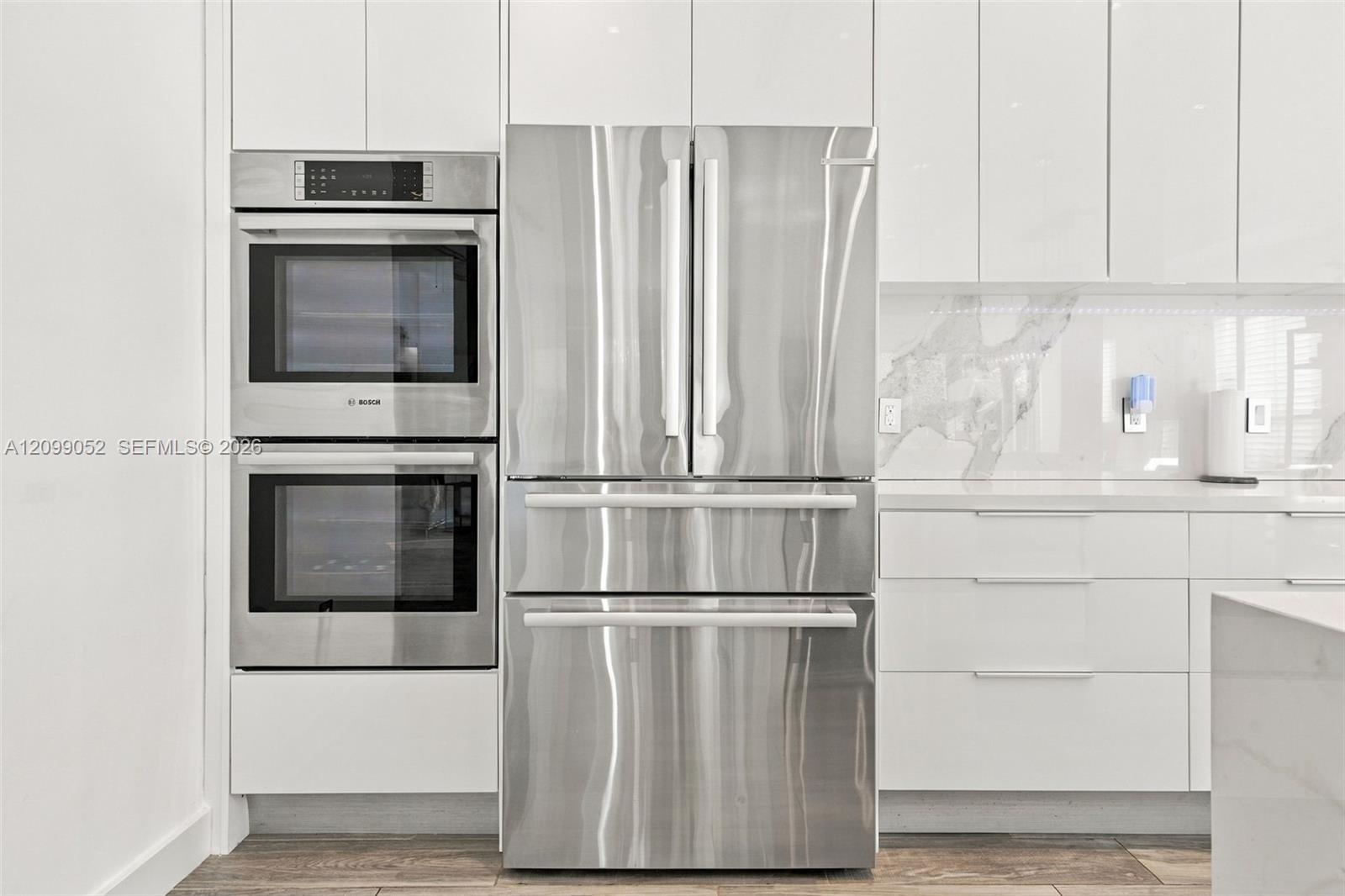 Kitchen featuring high-gloss white cabinetry, stainless steel double wall ovens, a stainless steel French-door refrigerator, stone-composite backsplas