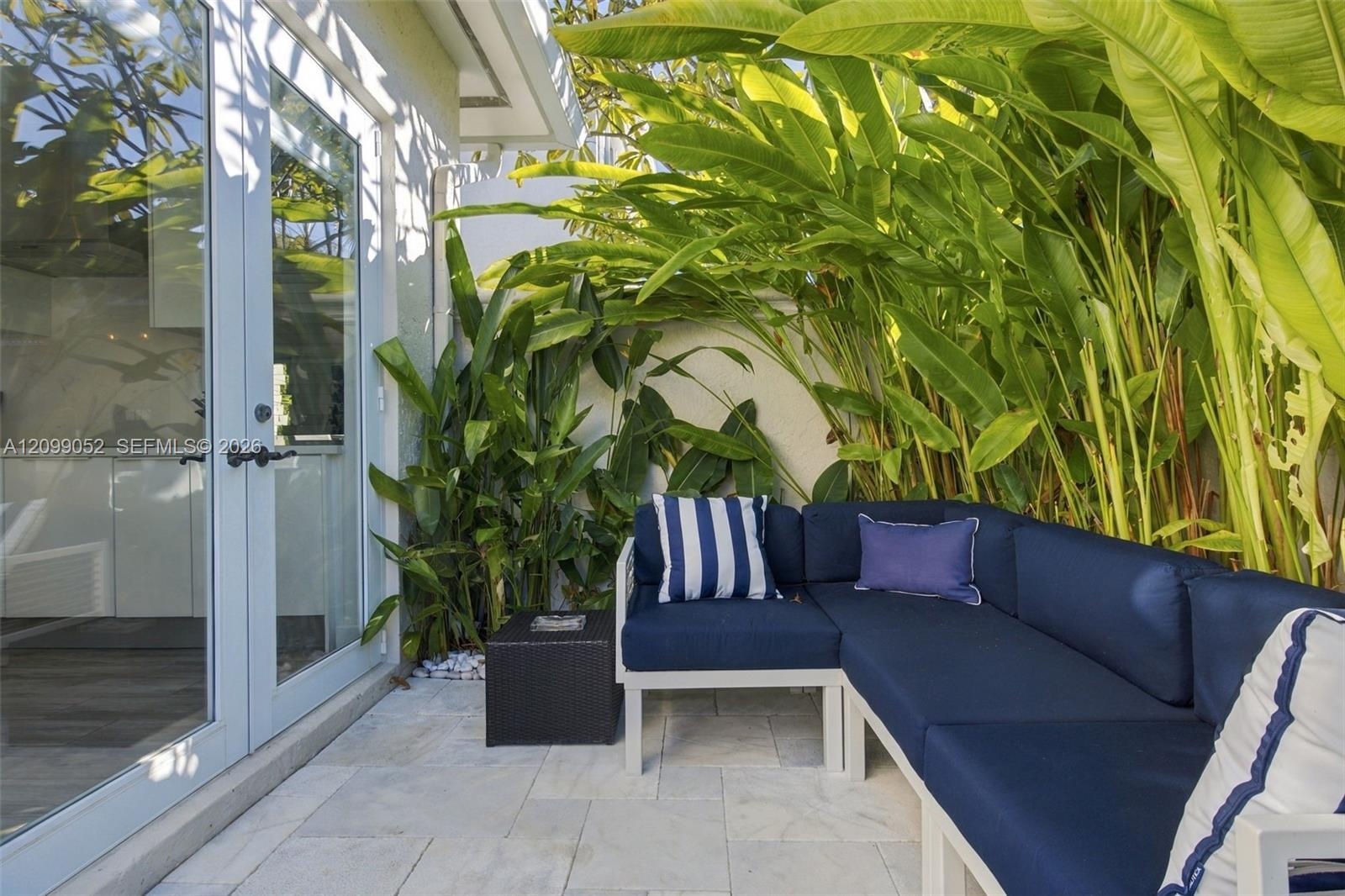 Outdoor patio featuring natural stone pavers, double-glass swing doors, and perimeter privacy wall with lush tropical greenery