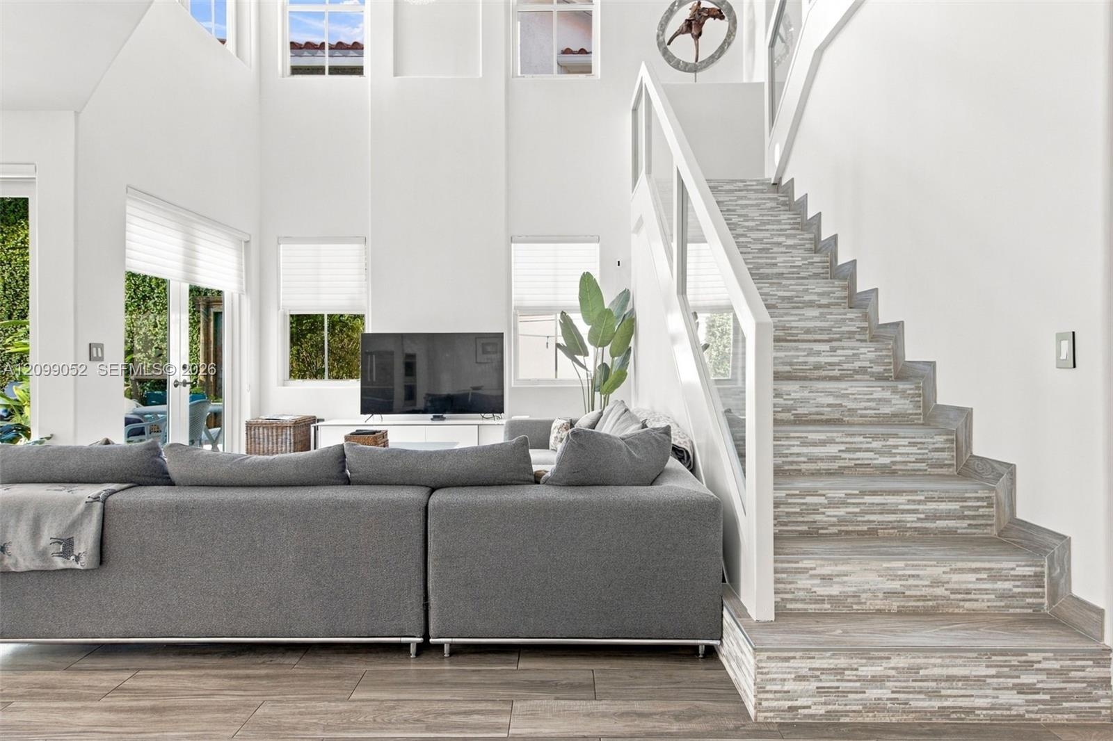 Double-height ceiling, open floor plan featuring wood-finish flooring, staircase with tiled risers, white railing, and glass paneled walls, and multip