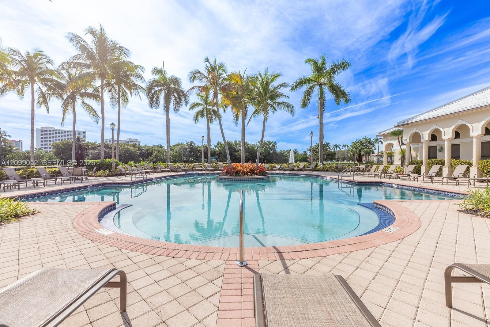 In-ground swimming pool featuring a curved perimeter, stepped entry, central garden island, and surrounding paver patio with a colonnade structure