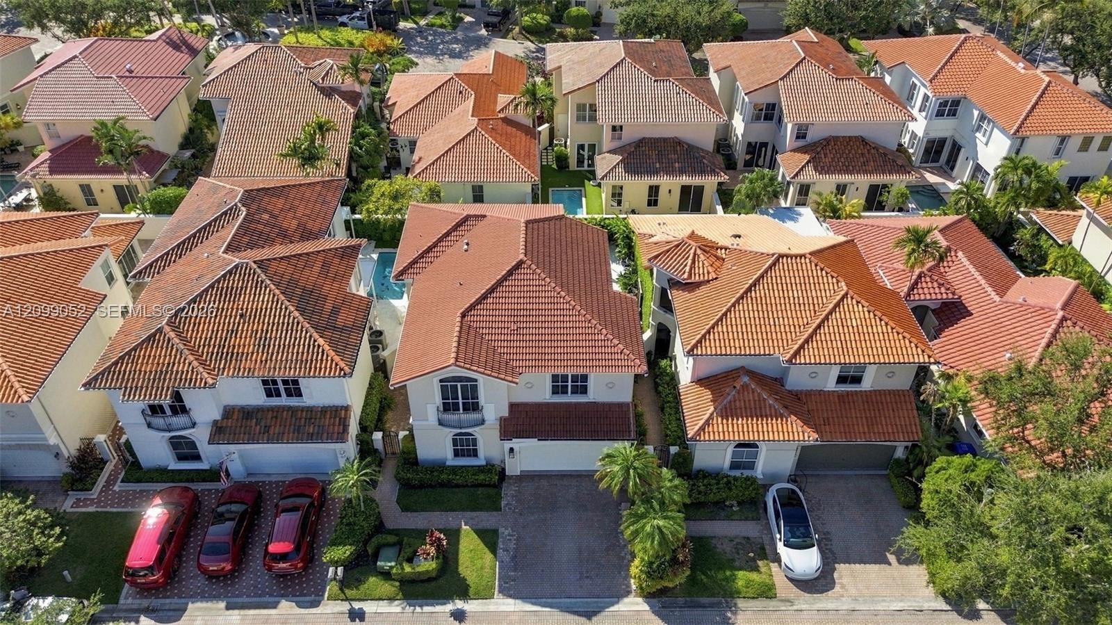 Aerial perspective of a multi-story residence featuring a terracotta-style tile roof, stucco exterior, integrated garage, and private pool