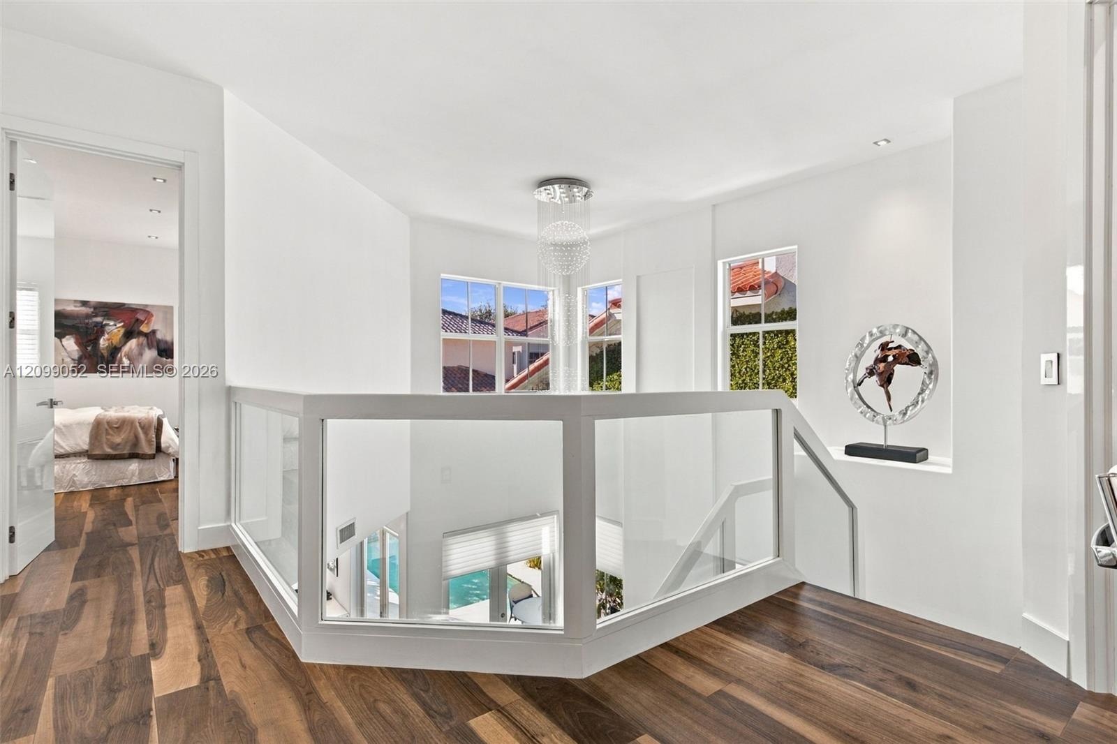 Landing featuring wood-finish flooring, glass panel railing, recessed ceiling lighting, and a tiered crystal chandelier