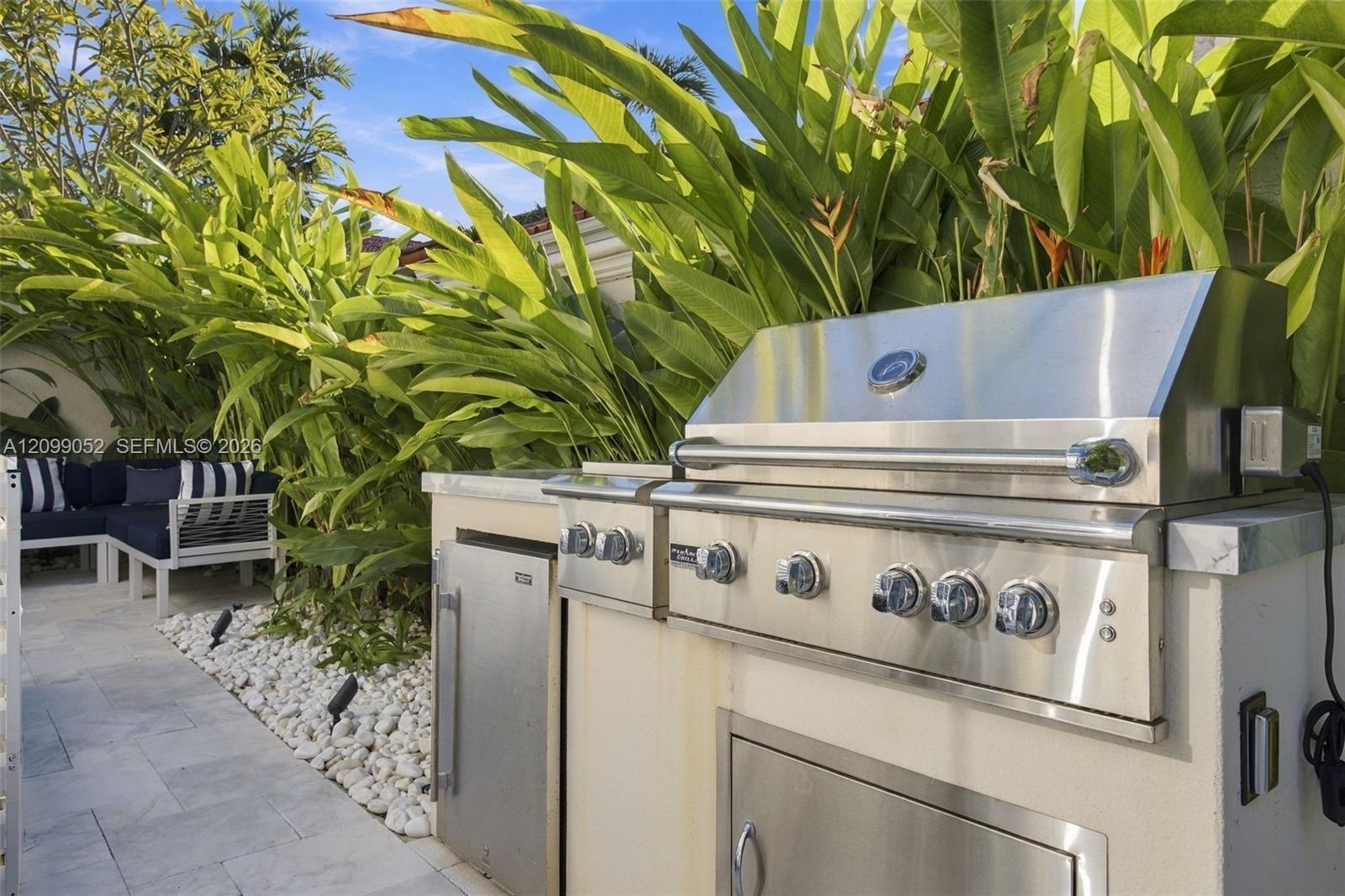 Outdoor kitchen featuring a stainless steel grill, stone-surfaced countertops, custom built-in cabinetry, and integrated storage, set against a landsc