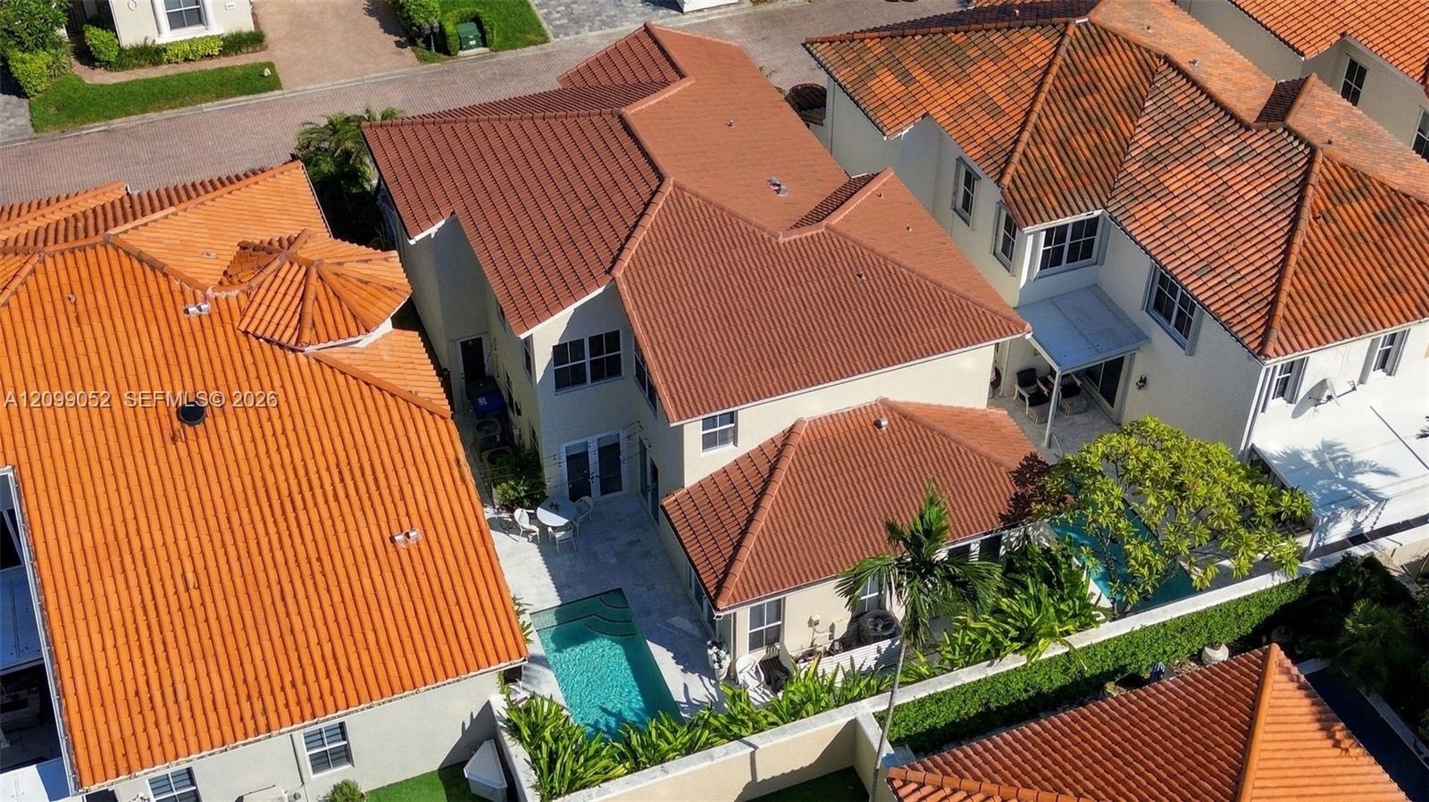 Aerial perspective of a multi-story residence featuring a terracotta-style tile roof, a private swimming pool, and a walled rear perimeter