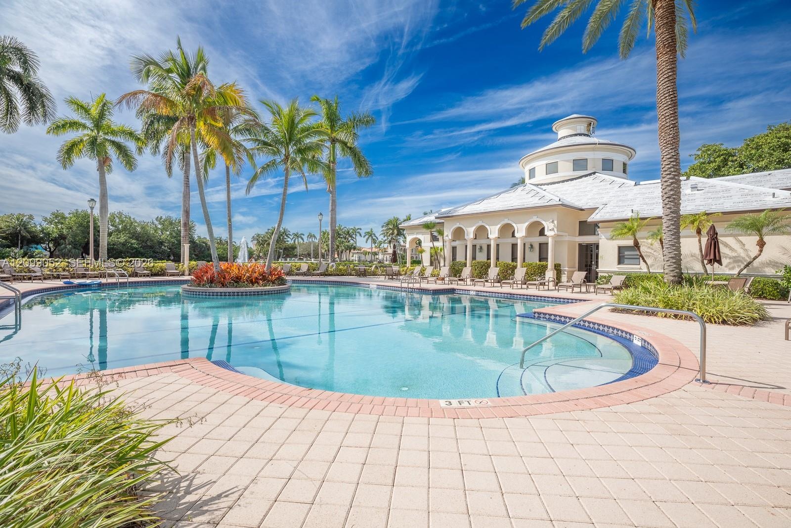 Swimming pool featuring a sun shelf entry, brick paver coping, and a central landscaped island with palm trees