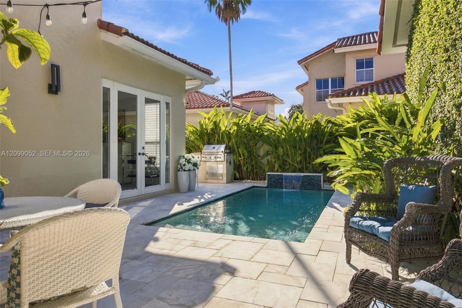 Outdoor living space featuring a tiled patio, private swimming pool with a stone-accented water feature, built-in stainless steel grill, and manicured