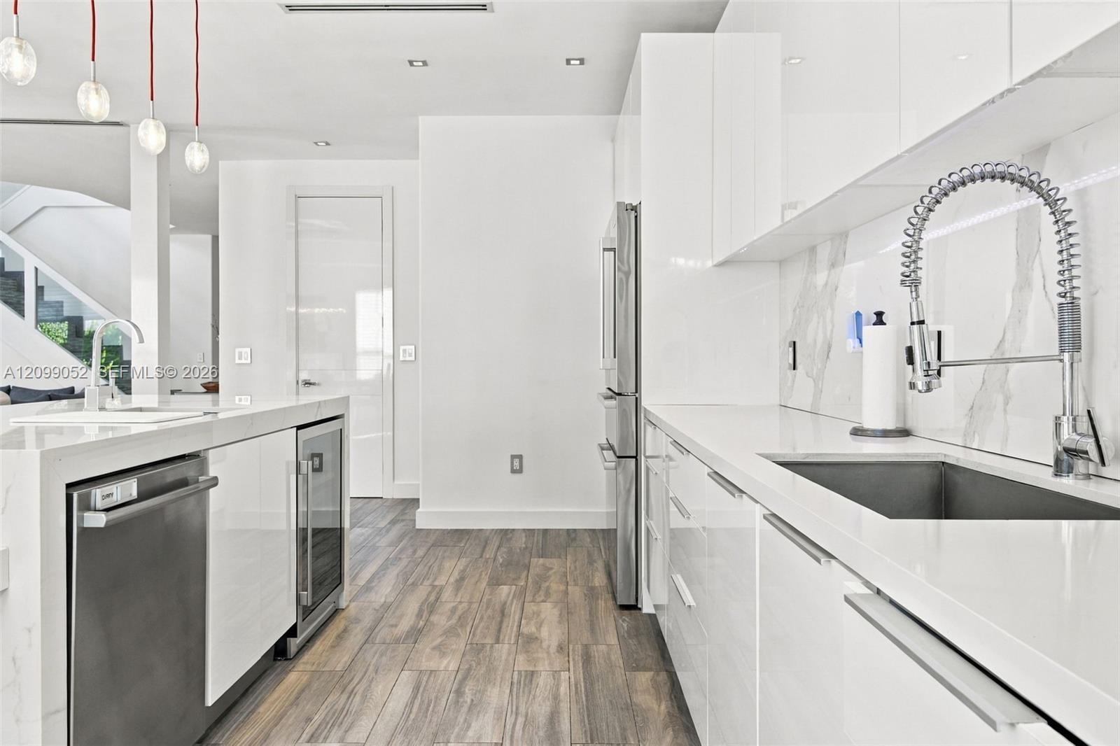 Kitchen featuring high-gloss white cabinetry, white stone countertops, integrated stainless steel appliances, a pull-down commercial-style faucet, and