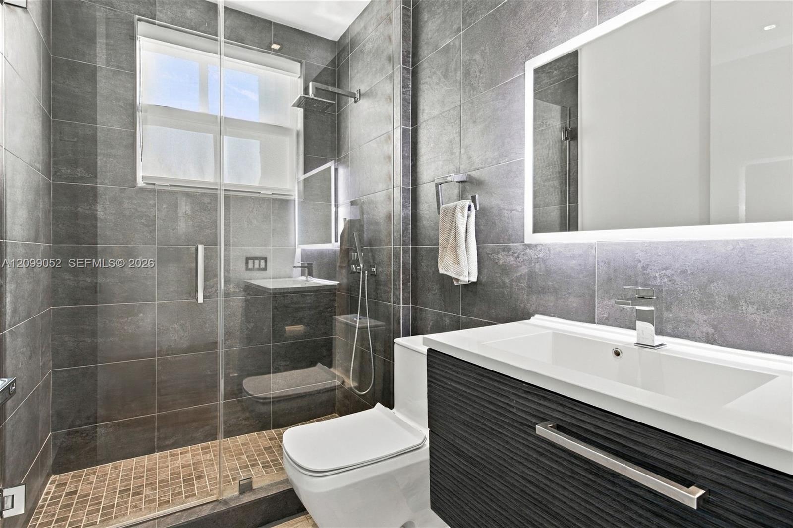 Bathroom featuring large-format dark grey wall tile, a glass-enclosed shower with a rainfall showerhead, a floating vanity with a textured cabinet fin
