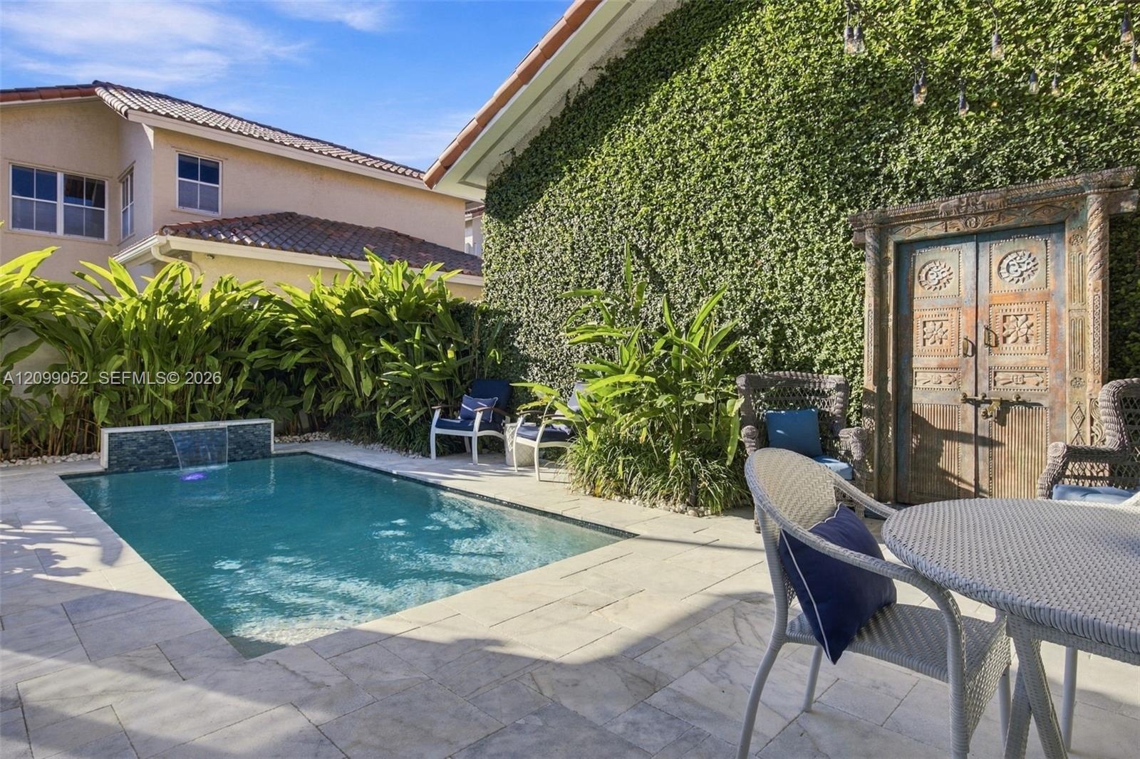 Outdoor space featuring a swimming pool with a built-in water feature, stone paver decking, decorative wood-carved gate, and exterior wall with climbi