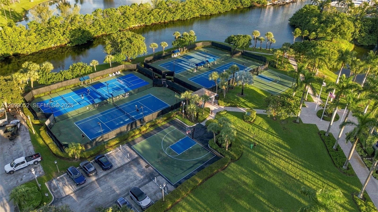 Recreational area featuring four tennis courts, a basketball court, paved walkways, and water frontage