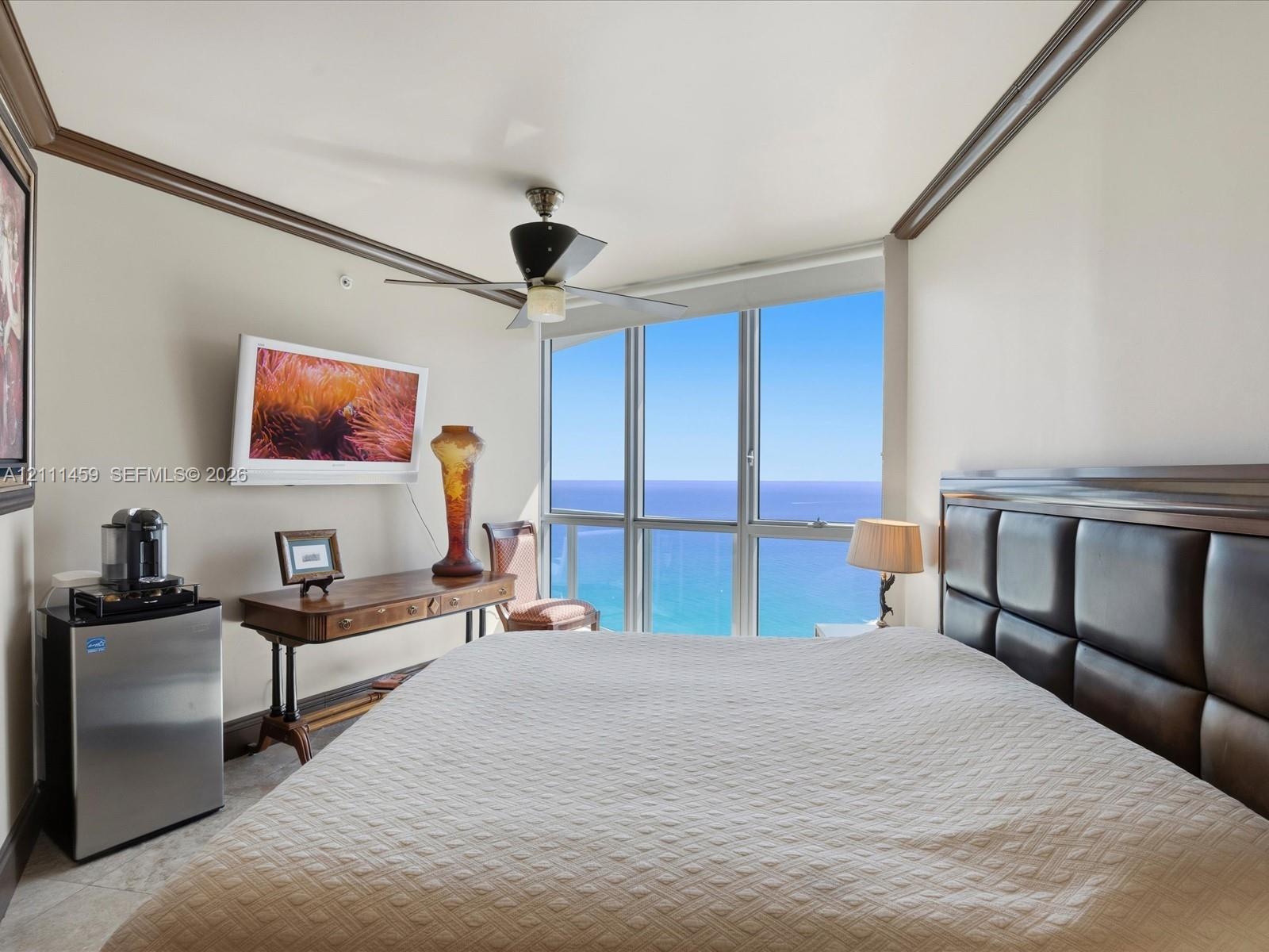 Floor-to-ceiling windows featuring ocean panoramas, crown molding, and a ceiling-mounted fan