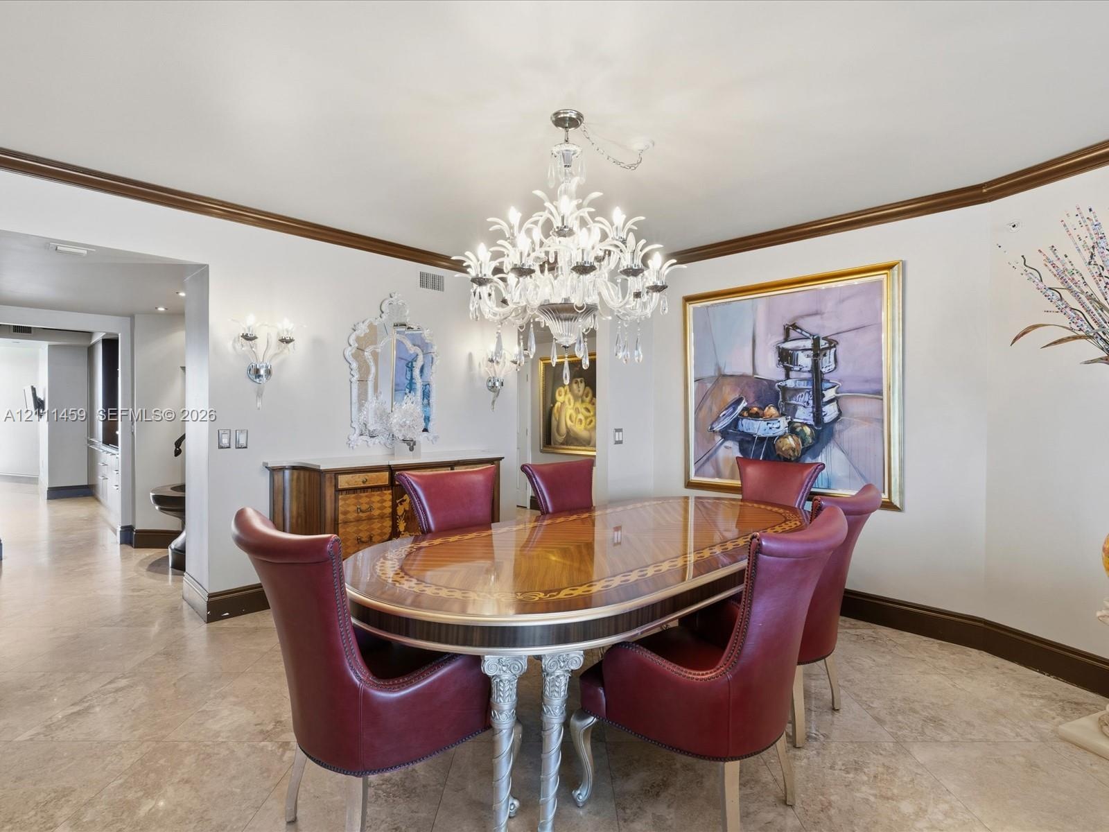 Ornate multi-tier crystal chandelier, built-in wooden sideboard with stone countertop, crown molding, stone tile flooring, and wall-mounted sconces