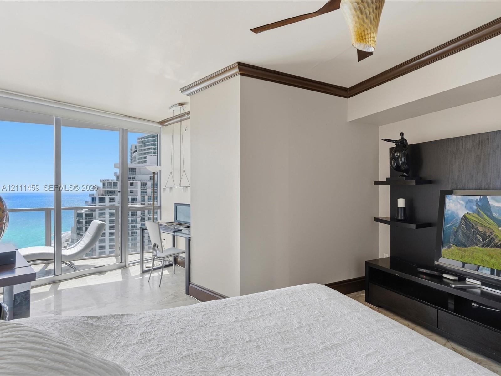 Floor-to-ceiling glass panel windows, built-in media console with tiered shelving, ceiling fan, crown molding, and polished stone flooring