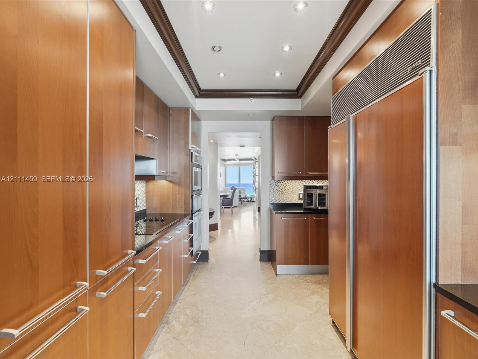 Galley kitchen featuring custom flat-panel wood cabinetry, integrated stainless steel refrigerator, black stone countertops, tile flooring, and recess