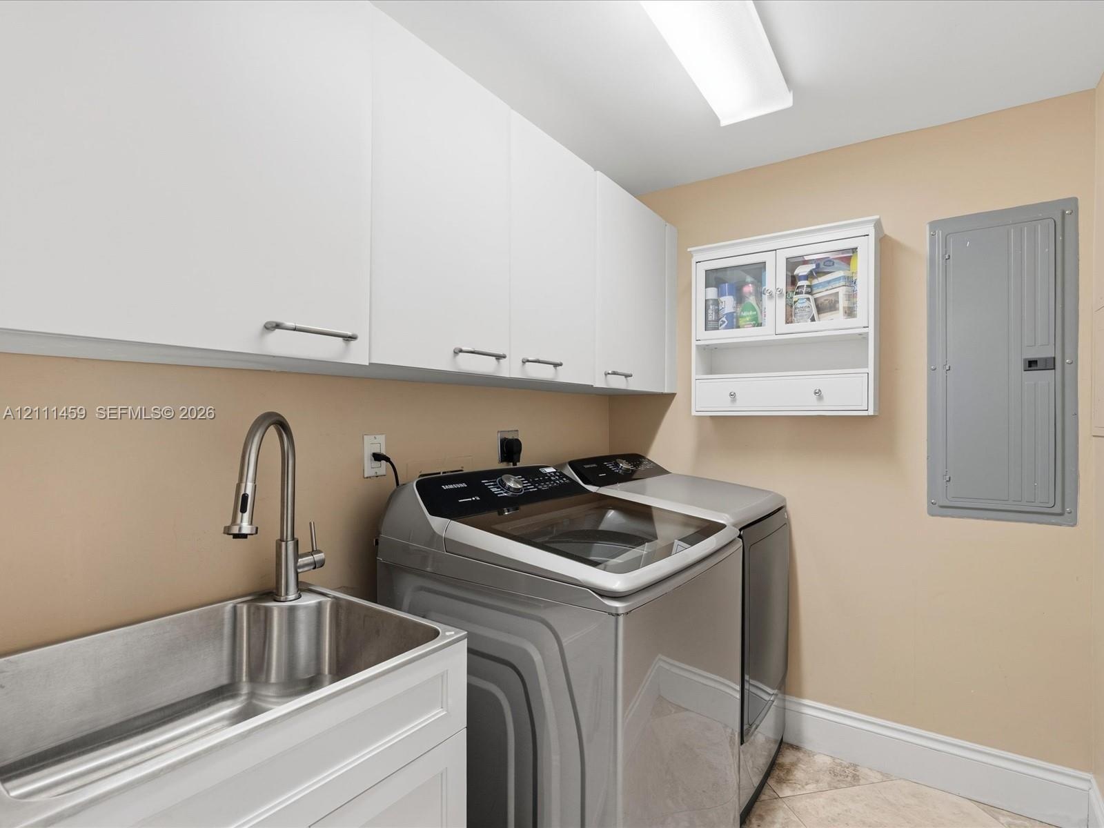 Laundry area featuring white shaker-style wall cabinets, a stainless steel utility sink with a high-arch pull-down faucet, and a wall-mounted glass-fr