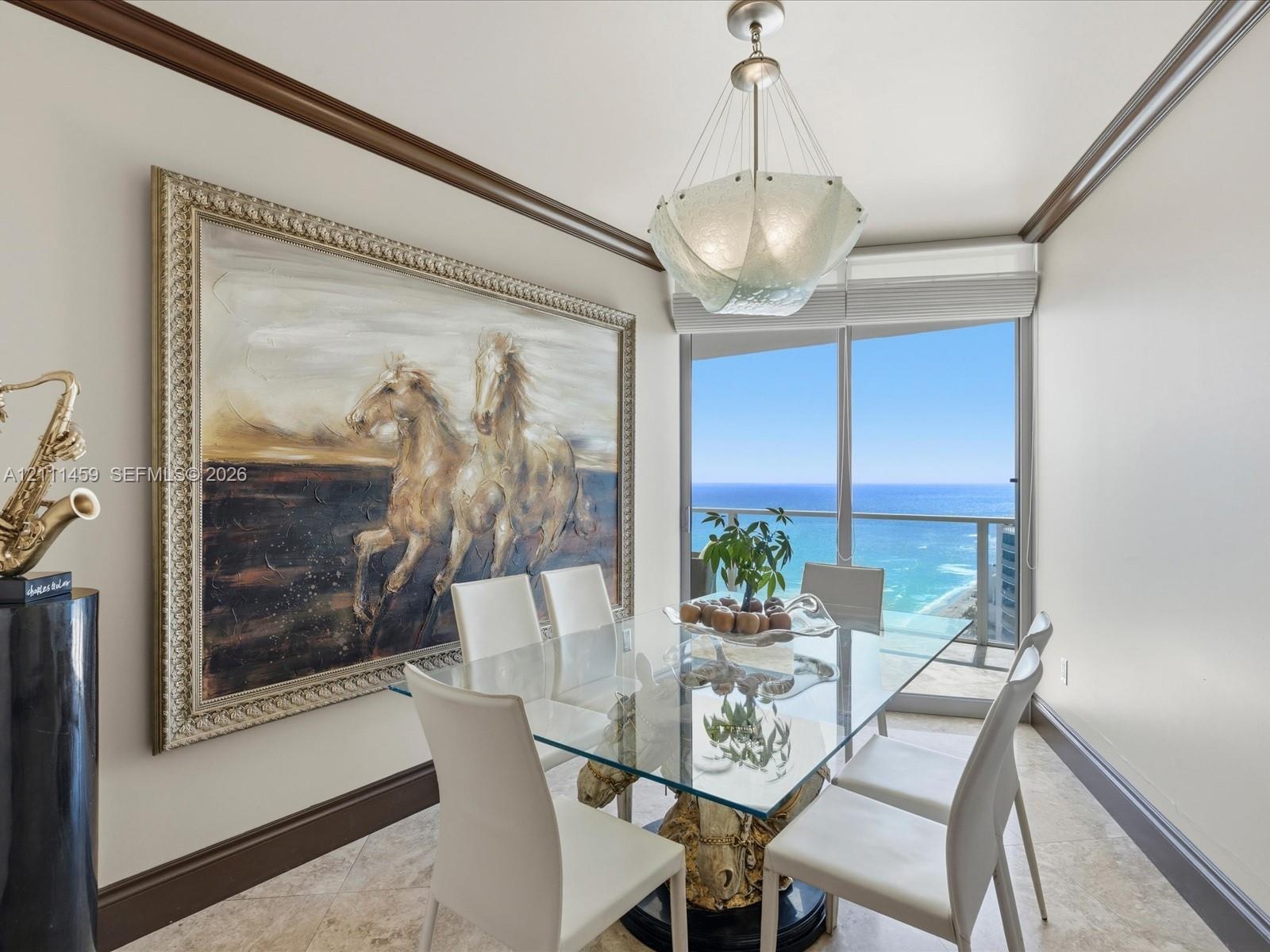 Dining space featuring stone tile flooring, crown molding, a custom pendant light fixture, and a floor-to-ceiling glass door opening to an oceanfront 
