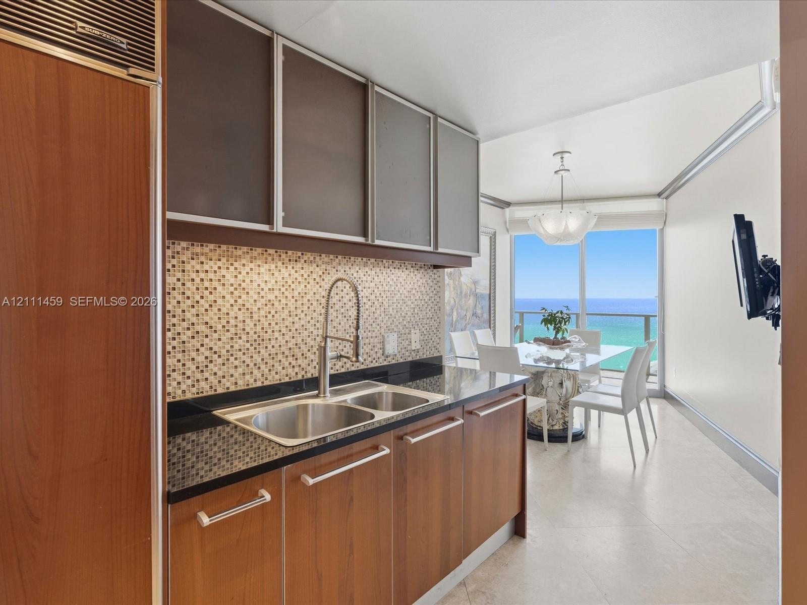 Kitchen featuring wood-finish cabinetry, a mosaic tile backsplash, dark solid-surface countertops, an integrated stainless steel refrigerator, and lar
