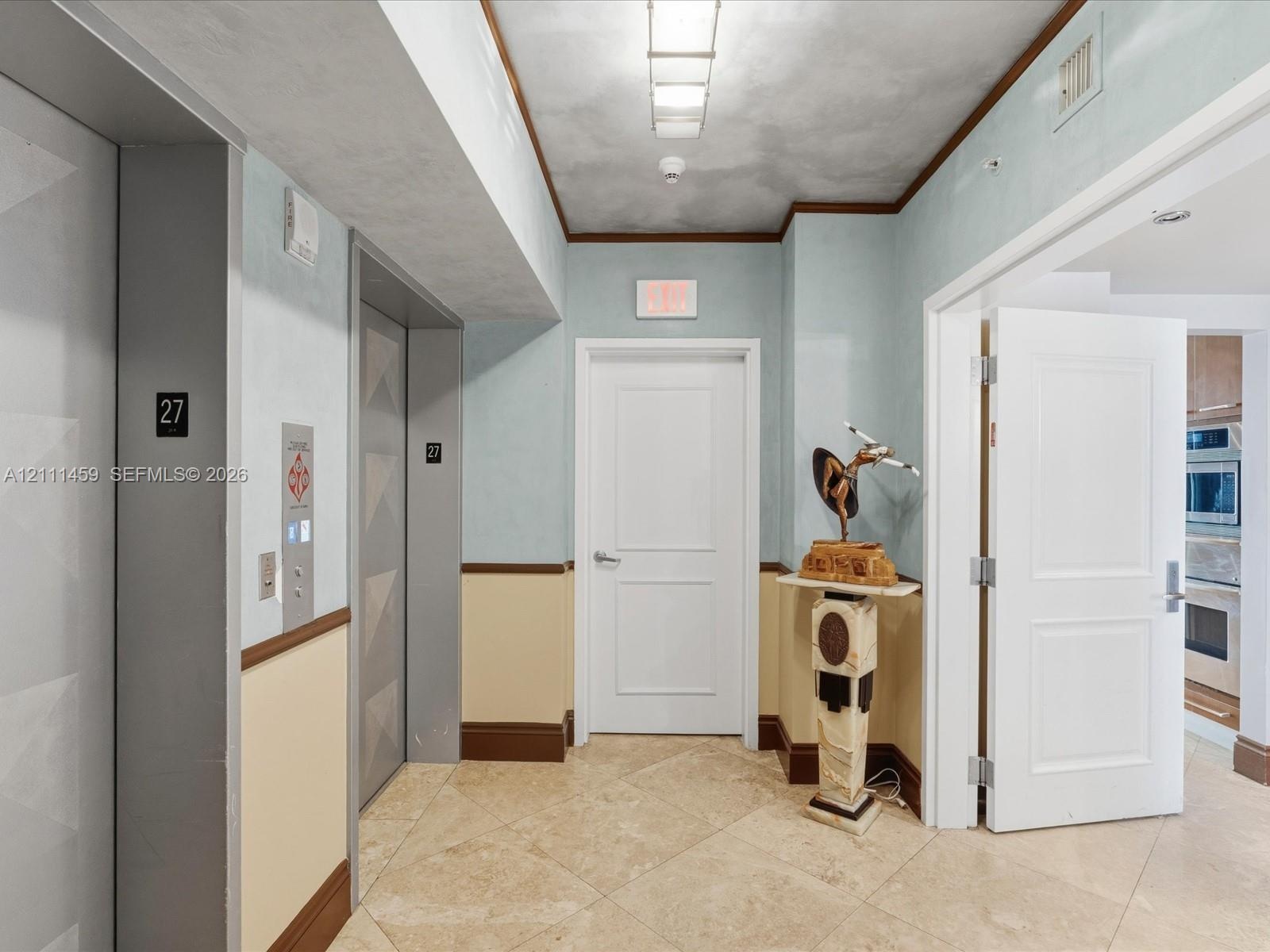 Foyer featuring stone-tile flooring, dual elevator access, painted wainscoting, and crown molding