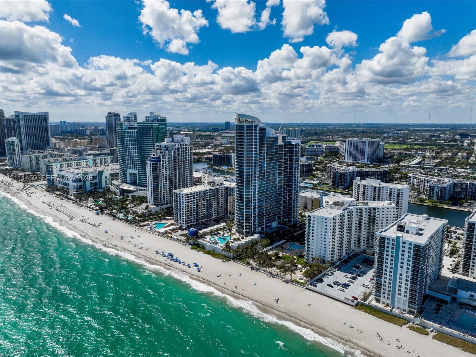 Aerial perspective of a coastal high-rise district featuring direct sandy shoreline access, multiple oceanfront structures, and extensive metropolitan