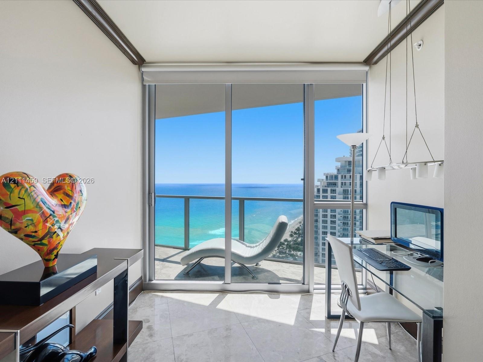 Floor-to-ceiling sliding glass doors, private balcony, neutral stone-finish flooring, and multi-pendant lighting fixture