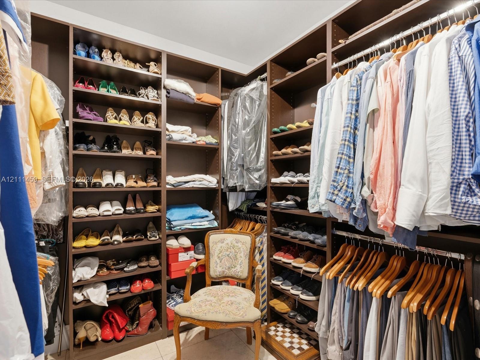 Walk-in closet featuring extensive dark wood-finish cabinetry, floor-to-ceiling adjustable shelving, integrated garment hanging rods, and tile floorin