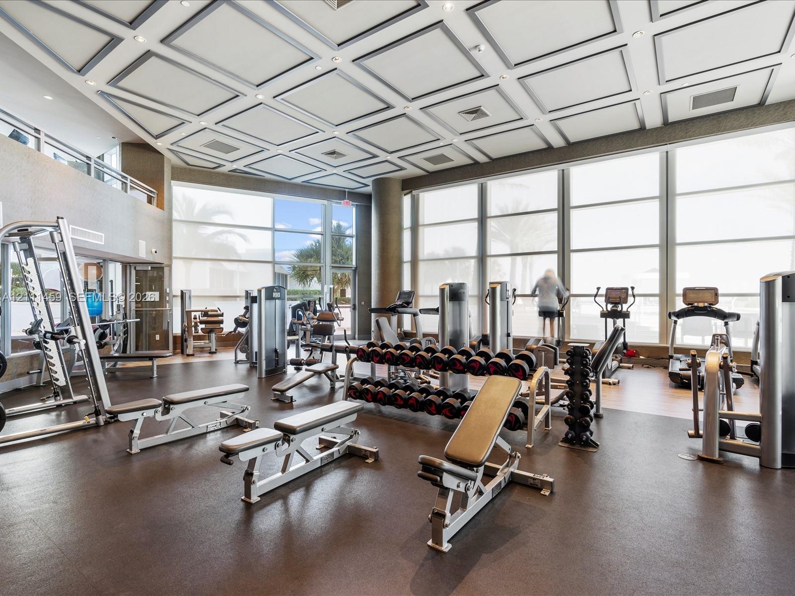 Fitness center featuring a coffered ceiling, floor-to-ceiling windows, and impact-resistant rubber flooring