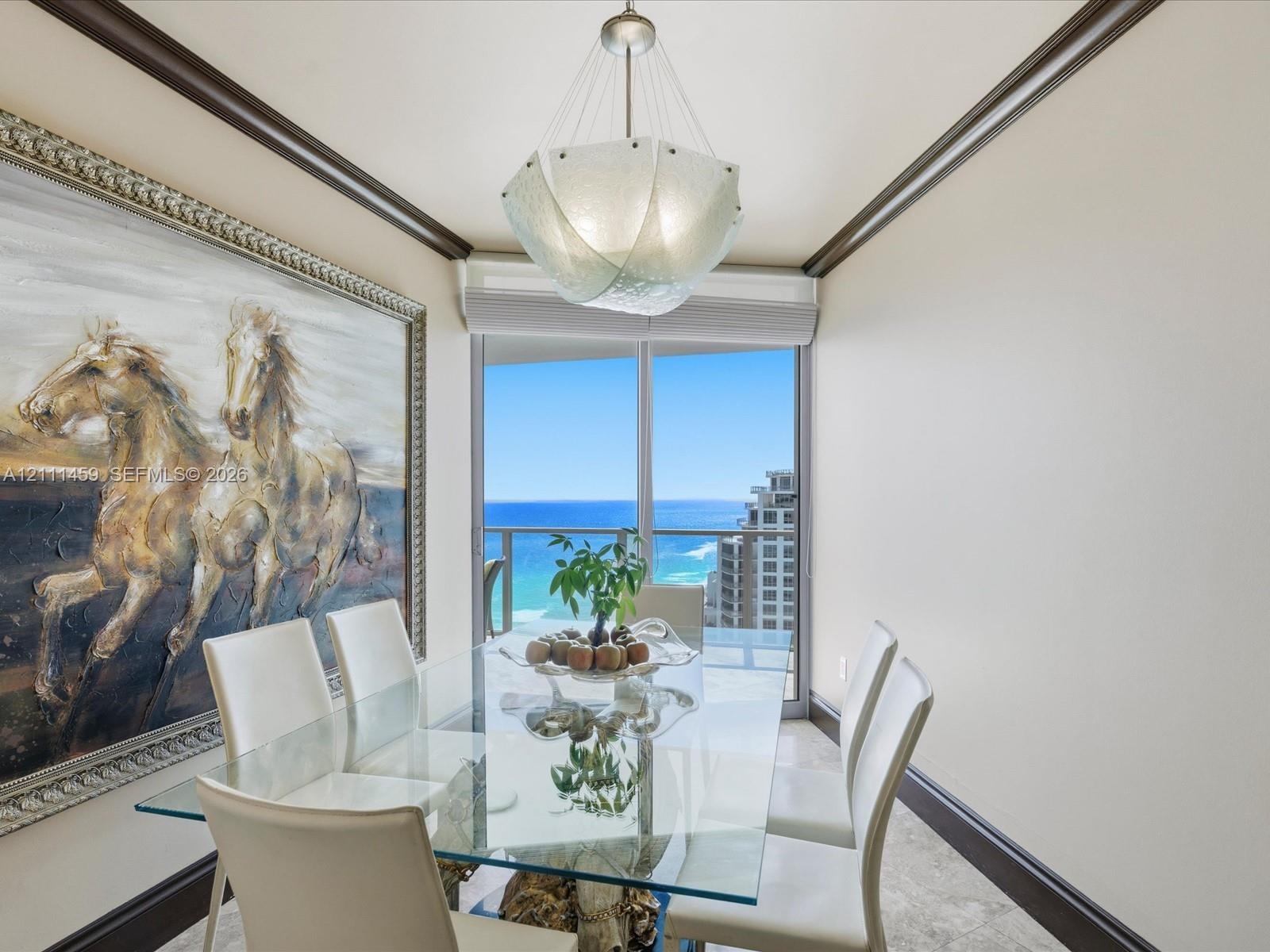 Dining space featuring dark crown molding, stone-finish flooring, a textured glass pendant light, and floor-to-ceiling glass doors opening to a balcon