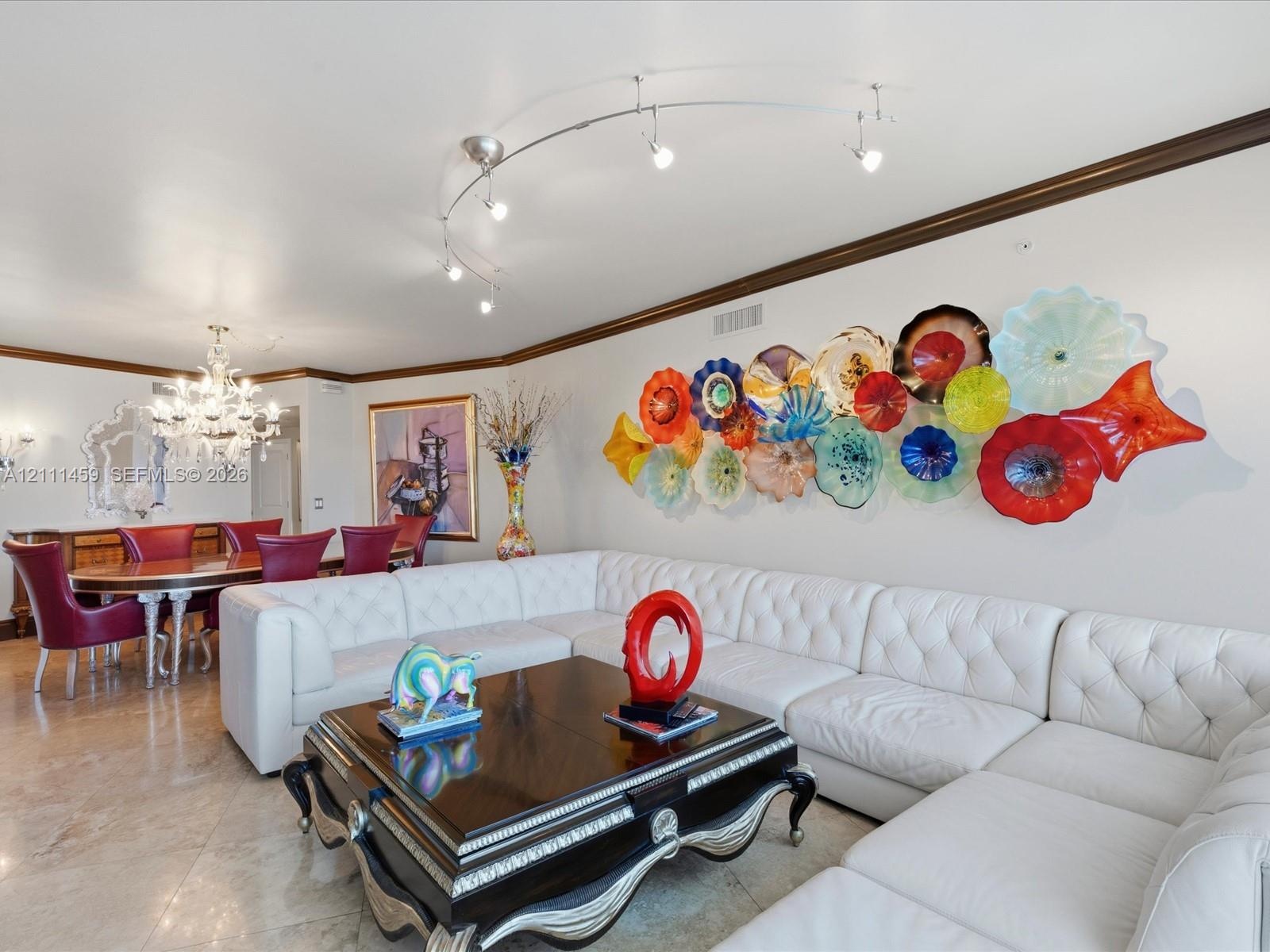 Polished stone flooring, crystal chandelier, curved track lighting, and decorative crown molding