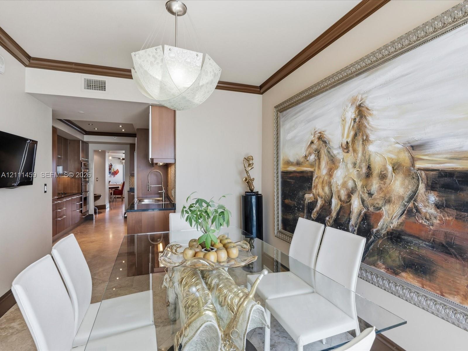 Dining area featuring crown molding, neutral wall finishes, stone tile flooring, and a decorative pendant light fixture