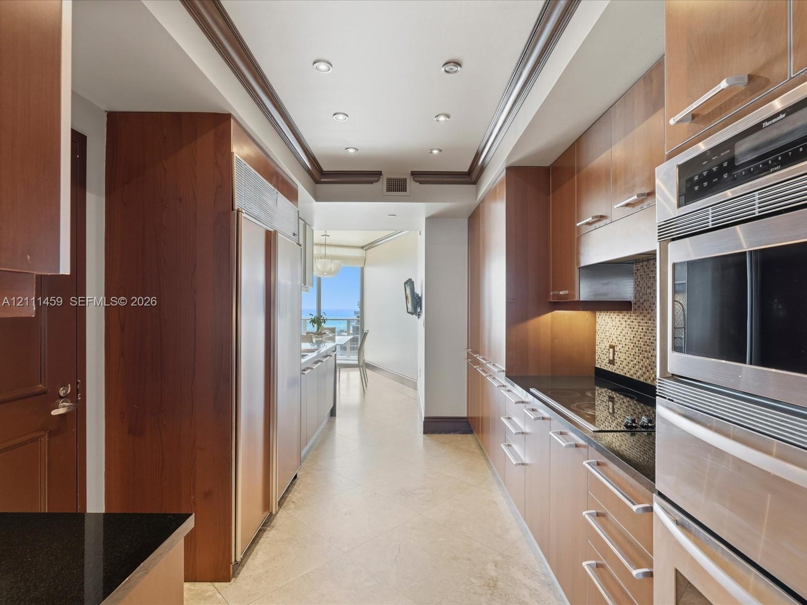 Galley kitchen featuring custom flat-panel wood cabinetry, black stone countertops, integrated stainless steel refrigeration, built-in double ovens, a