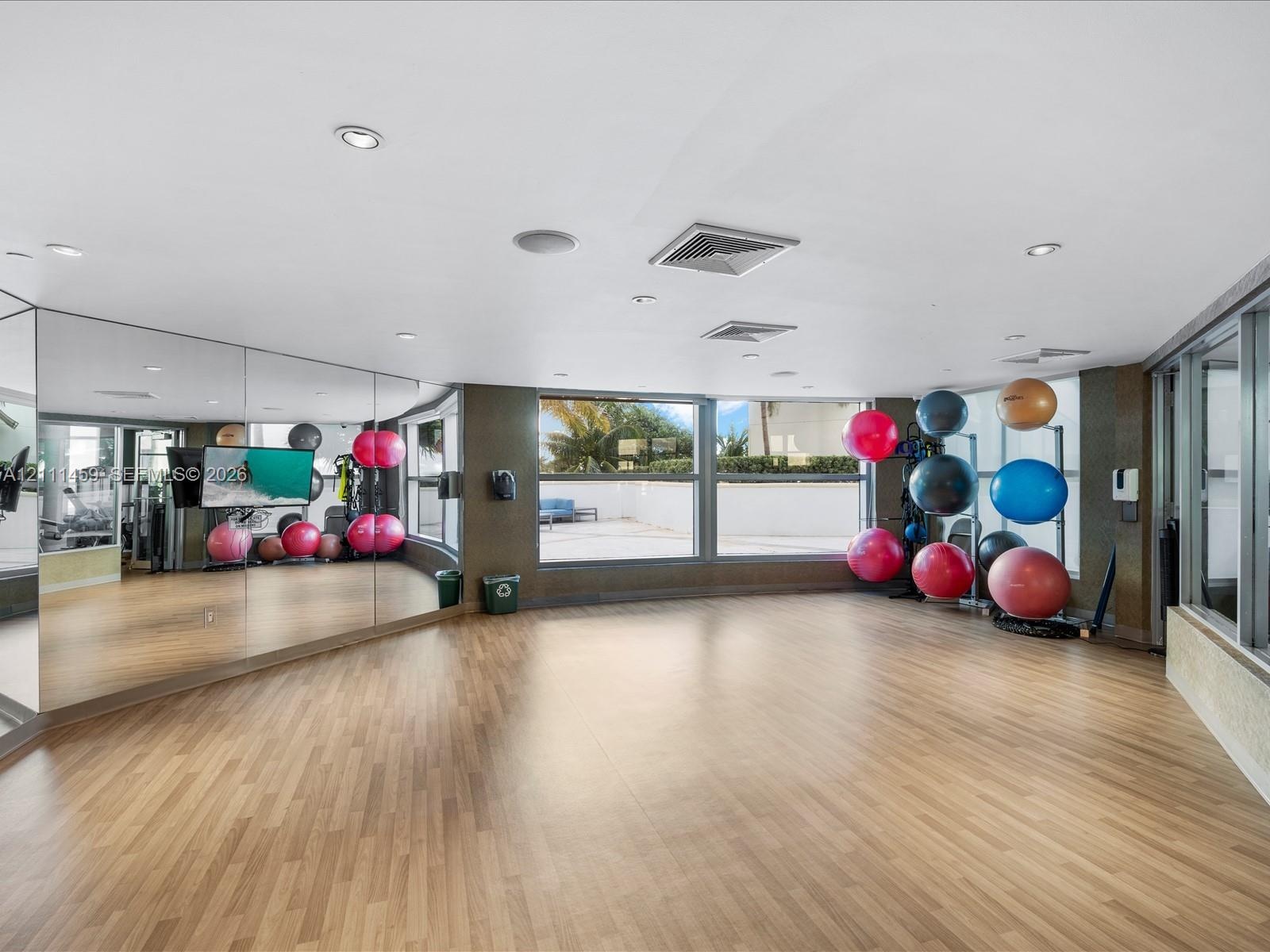 Fitness room featuring wood-finish flooring, full-length wall mirrors, recessed lighting, and expansive windows