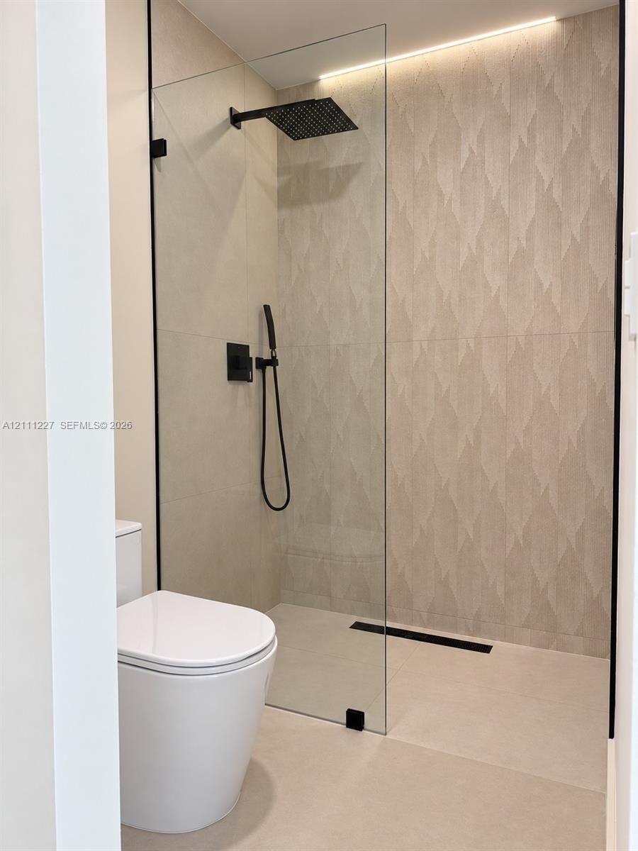Walk-in shower featuring a frameless glass enclosure, patterned tile accent wall, matte black rainfall showerhead, integrated handheld sprayer, and li